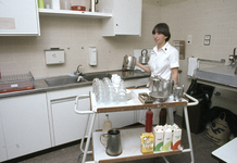 828100 Afbeelding van een leerling-verpleegkundige die de lunch voor patiënten aan het voorbereiden is, in een keuken ...